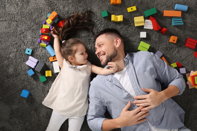 Photo of Father and daughter lying on floor at home, top view. Playing with children