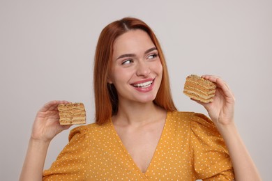 Photo of Young woman with pieces of tasty cake on light grey background