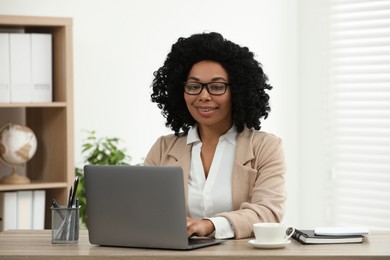 Photo of Happy young woman using laptop at wooden desk indoors