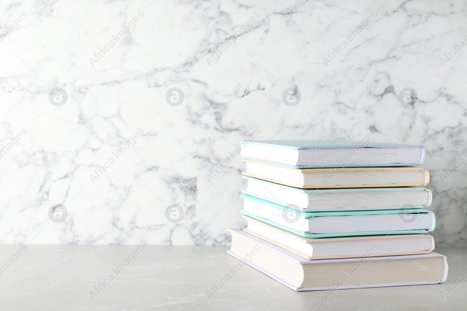 Photo of Stack of hardcover books on table against marble background, space for text