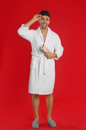 Photo of Happy young man in bathrobe with newspaper on red background
