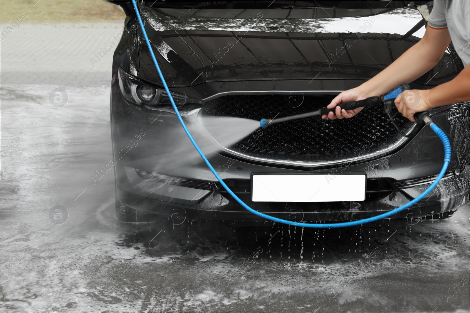 Photo of Man washing auto with high pressure water jet at car wash, closeup