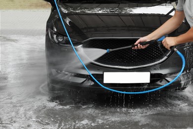 Man washing auto with high pressure water jet at car wash, closeup