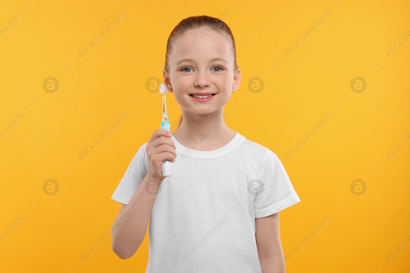 Photo of Happy girl holding electric toothbrush on yellow background