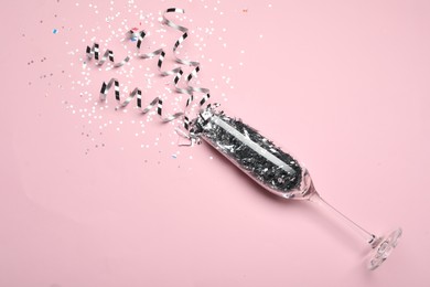 Photo of Glass and shiny confetti on pink background, above view