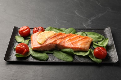 Photo of Tasty grilled salmon with tomatoes, spinach and lemon on black table