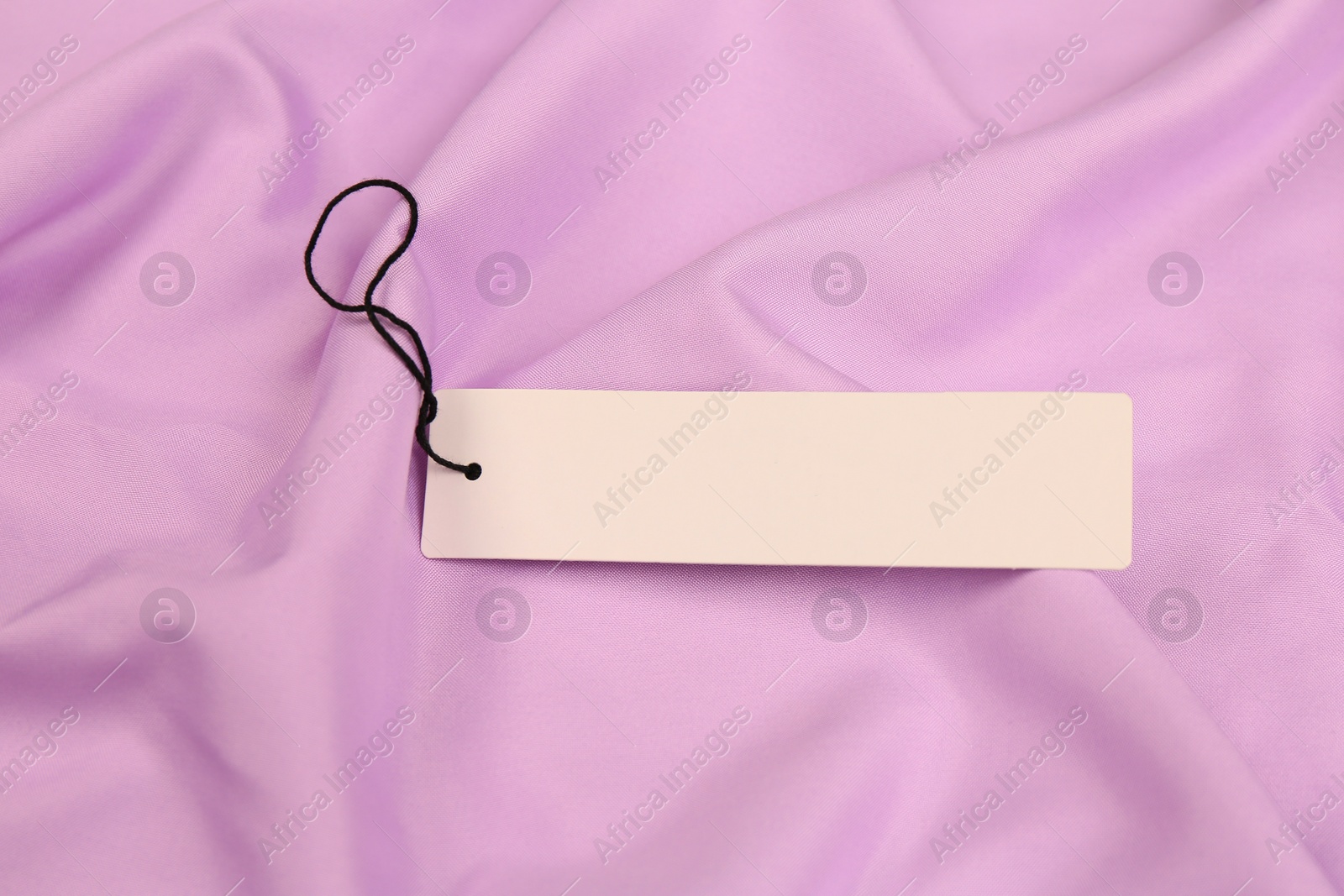 Photo of Blank white tag on violet fabric. Space or text