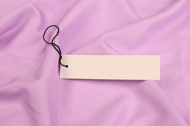 Photo of Blank white tag on violet fabric. Space or text