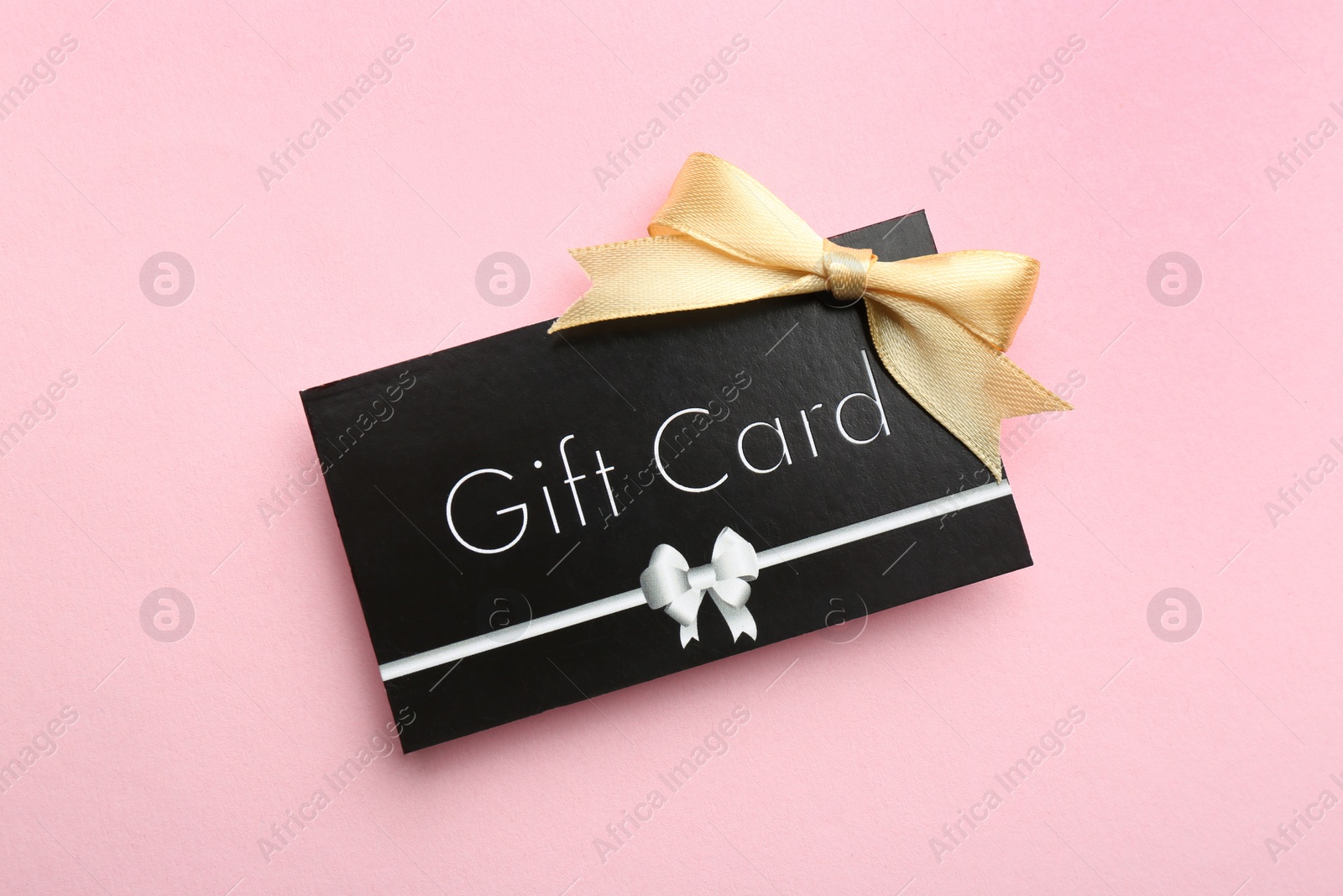 Photo of Gift card with bow on pink background, top view