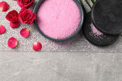 Natural sea salt in bowl, spa stones, rose flowers and petals on grey table, flat lay. Space for text