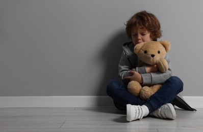 Photo of Child abuse. Upset boy with toy sitting on floor near grey wall, space for text