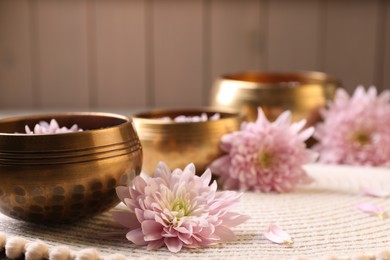 Tibetan singing bowls with water and beautiful flowers on table, space for text