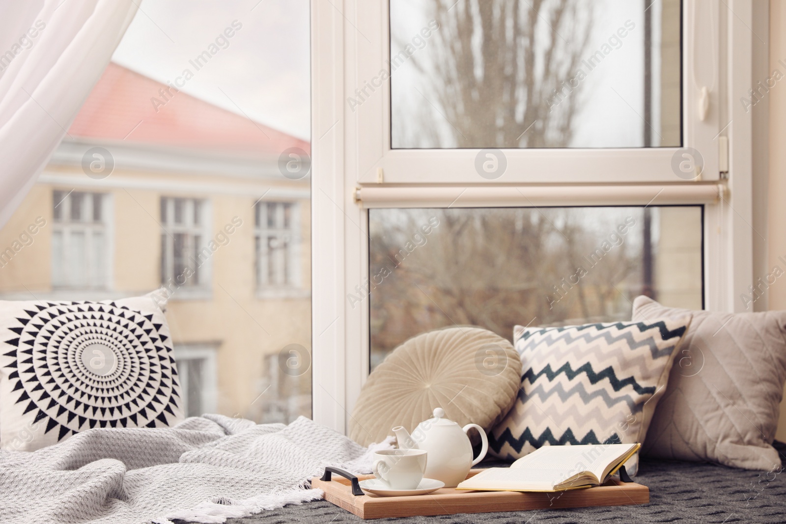 Photo of Comfortable lounge area with blanket and soft pillows near window in room