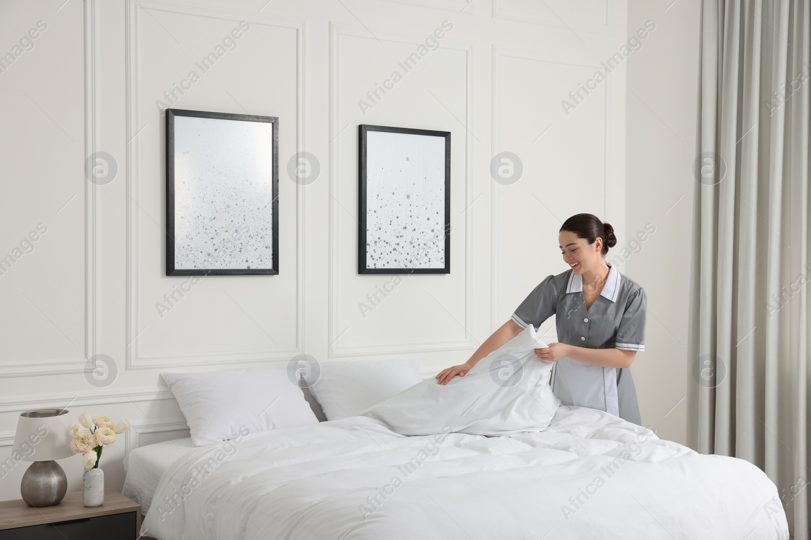 Photo of Young chambermaid making bed in hotel room. Space for text