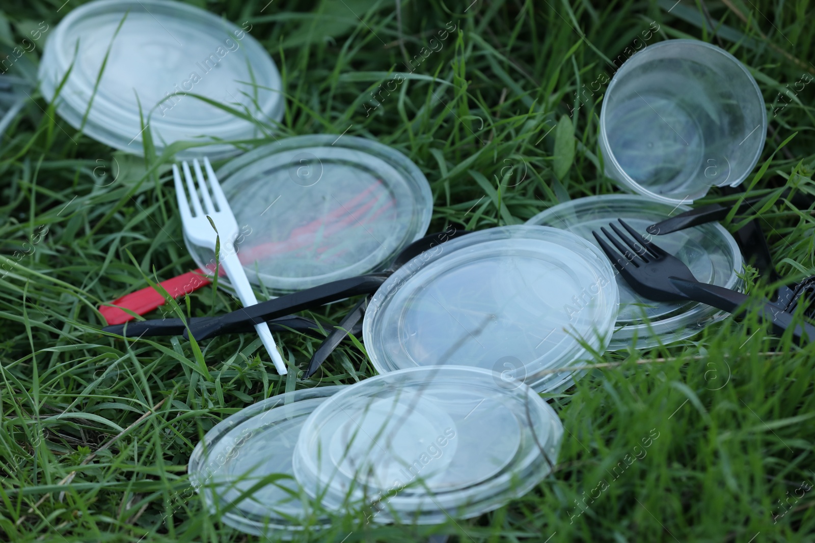 Photo of Used plastic tableware on grass outdoors, closeup. Environmental pollution concept