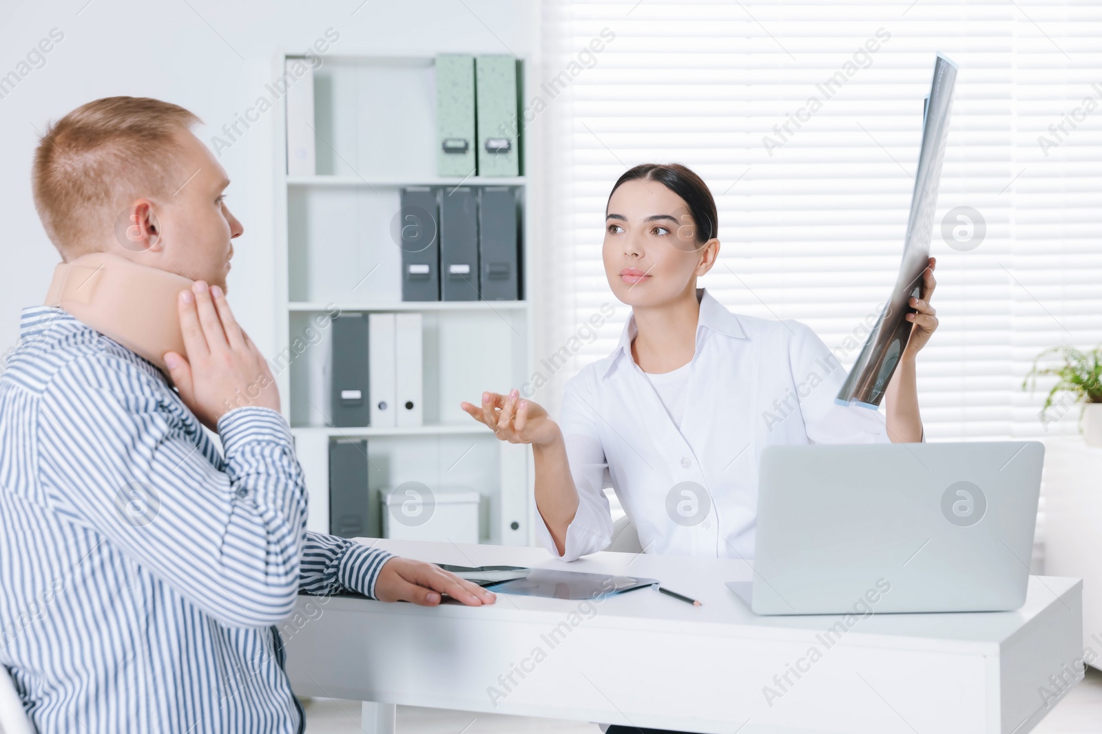 Photo of Doctor with neck MRI image consulting patient in clinic