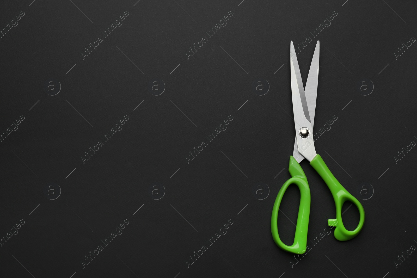 Photo of Pair of sharp scissors on dark background, top view. Space for text