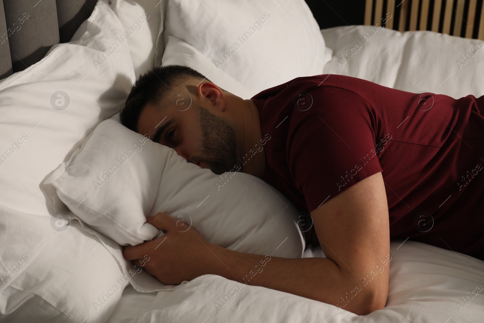 Photo of Sad man hiding face in pillow on bed at home