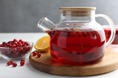 Photo of Tasty hot cranberry tea in teapot, lemon and fresh berries on white wooden table