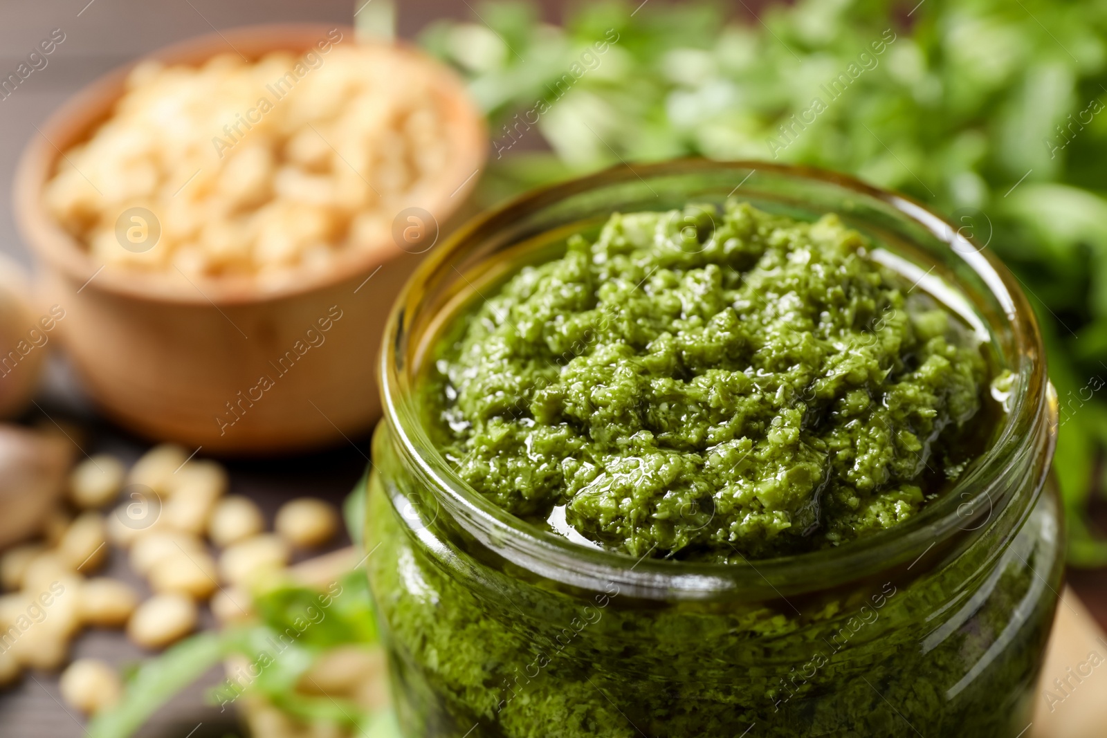 Photo of Jar of tasty arugula pesto on table, closeup