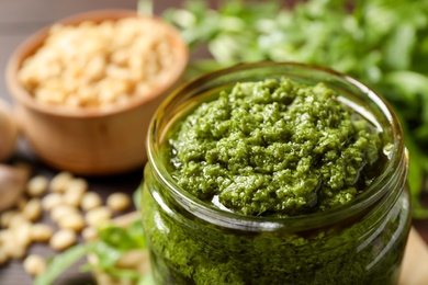 Photo of Jar of tasty arugula pesto on table, closeup