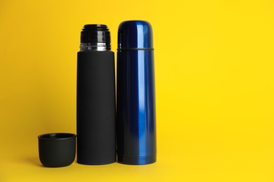 Photo of Stylish stainless thermo bottles on yellow background. Space for text