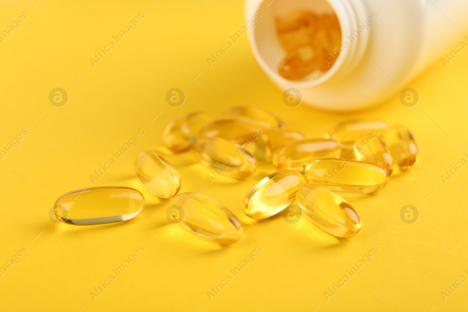 Photo of Vitamin capsules and medical bottle on yellow background, closeup