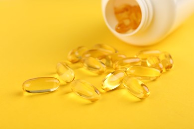 Vitamin capsules and medical bottle on yellow background, closeup