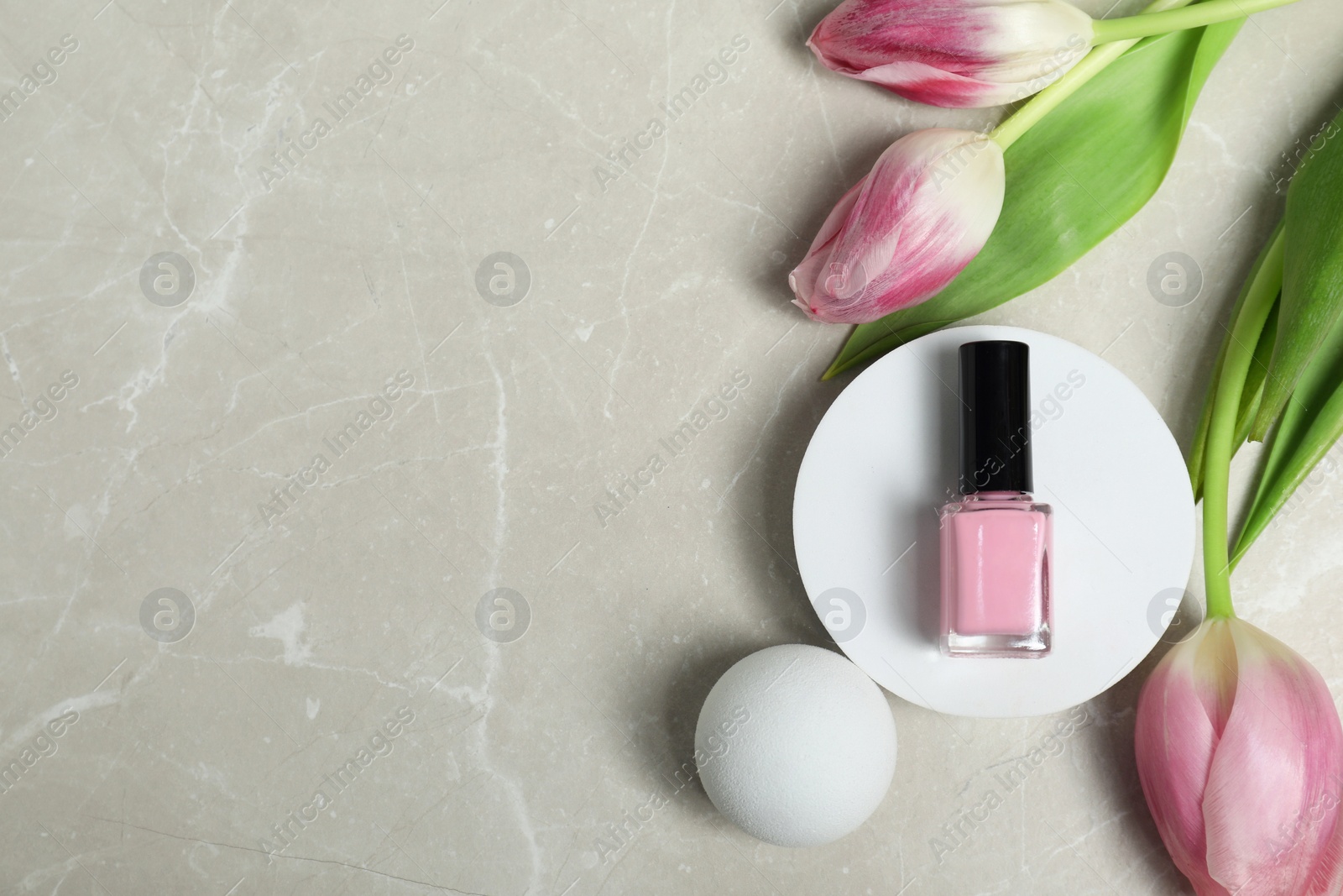 Photo of Flat lay composition with pink nail polish in bottle and tulip flowers on light textured table. Space for text