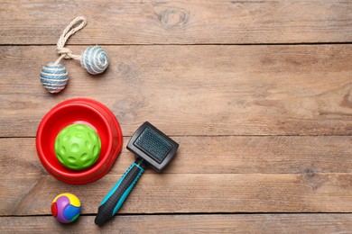 Photo of Pet toys, bowl and brush on wooden table, flat lay. Space for text