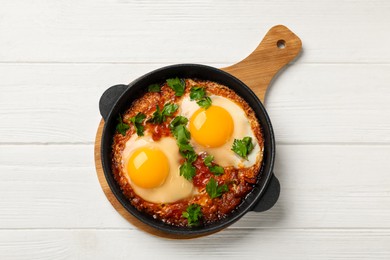 Delicious shakshuka in frying pan on white wooden table, top view