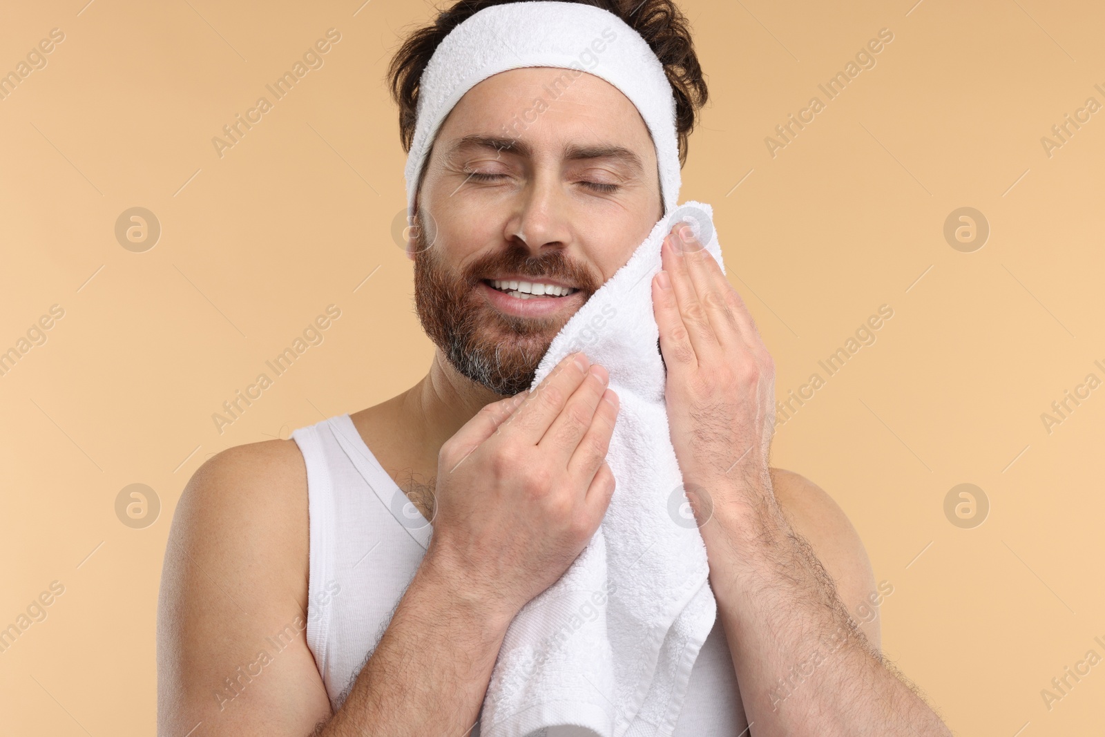 Photo of Washing face. Man with headband and towel on beige background