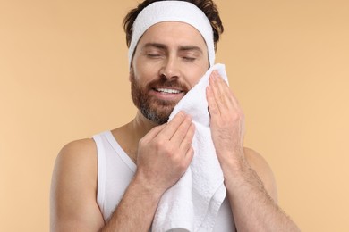 Photo of Washing face. Man with headband and towel on beige background