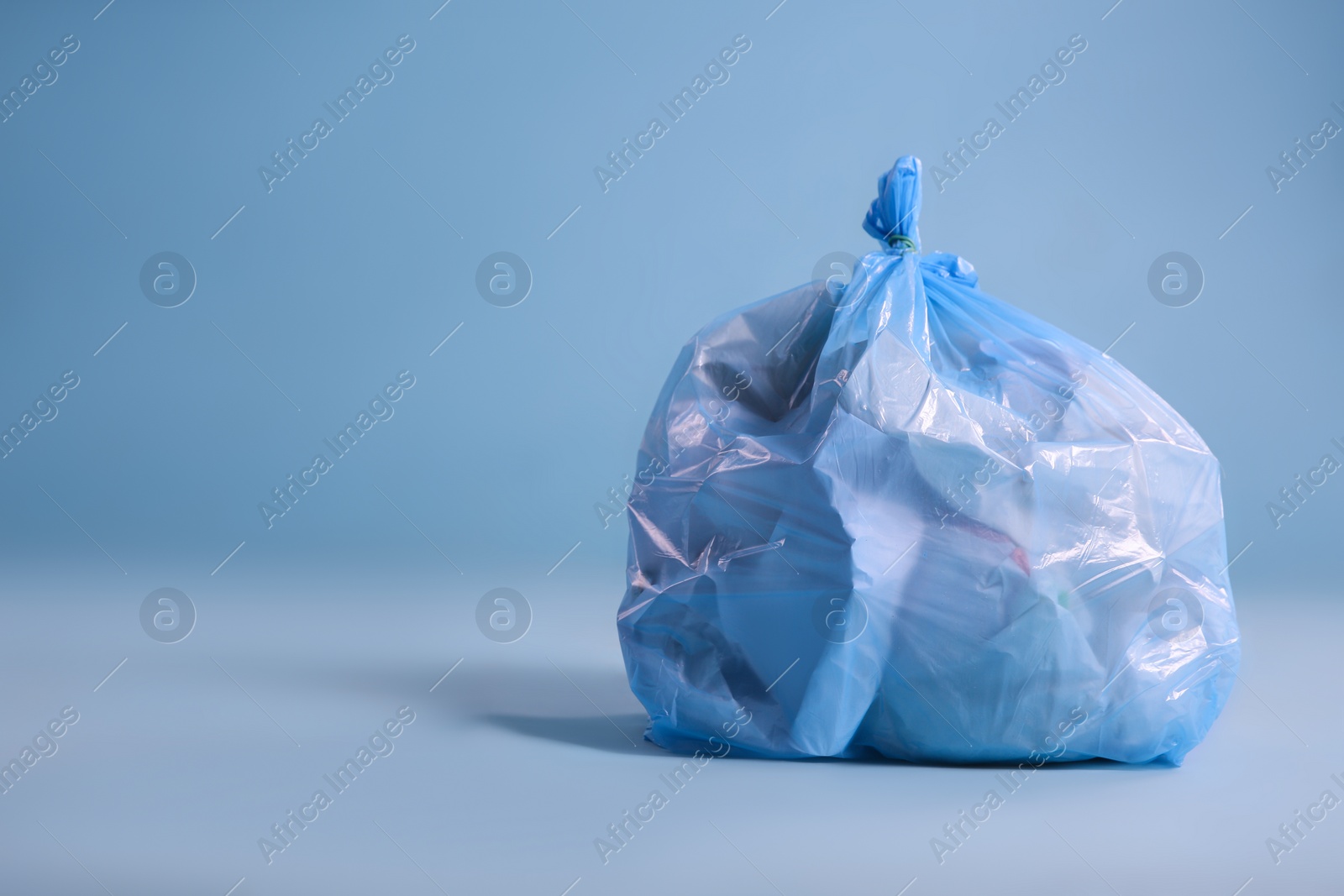 Photo of Trash bag full of garbage on light blue background, space for text