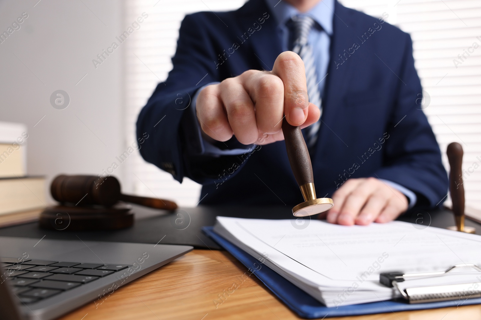 Photo of Notary stamping document at wooden table in office, closeup. Space for text