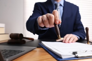 Notary stamping document at wooden table in office, closeup. Space for text