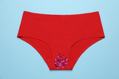 Woman's panties with pink sequins on light blue background, top view. Menstrual cycle