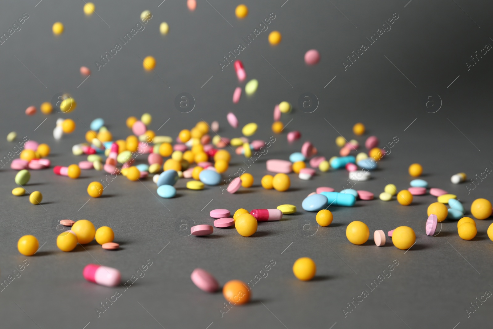 Photo of Different pills falling on table against gray background
