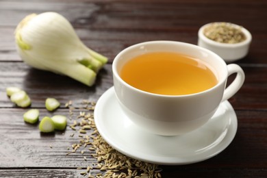 Photo of Fennel tea in cup, seeds and fresh vegetable on wooden table, closeup