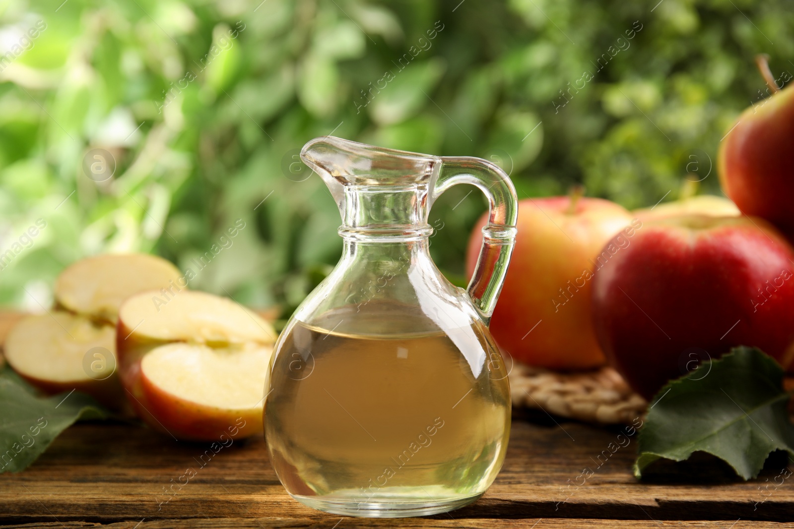 Photo of Natural apple vinegar and fresh fruits on wooden table against blurred background