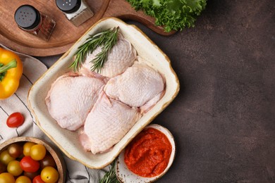 Flat lay composition with marinade, raw chicken, rosemary and other products on brown table. Space for text