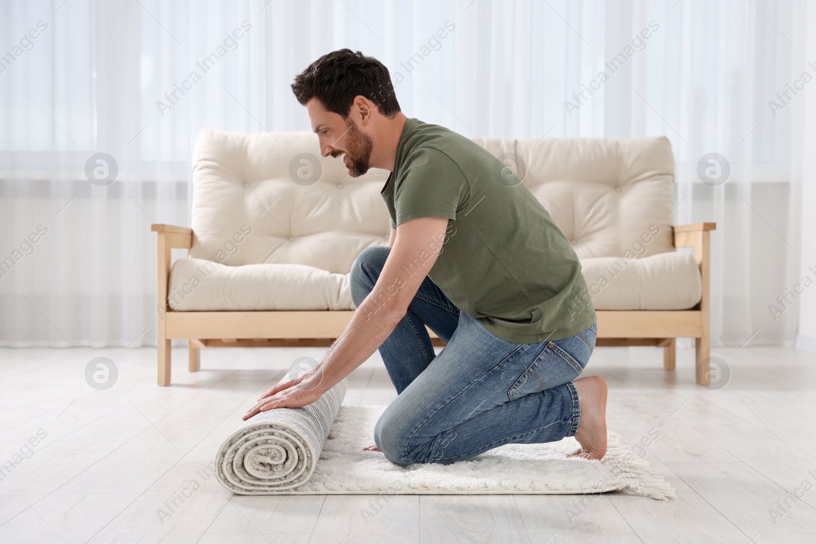 Photo of Smiling man unrolling carpet with beautiful pattern on floor in room