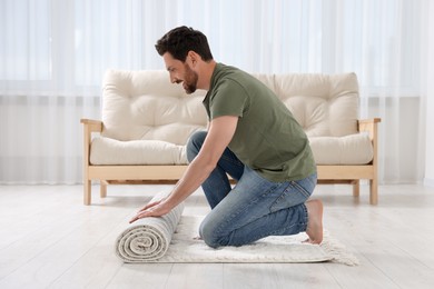 Photo of Smiling man unrolling carpet with beautiful pattern on floor in room