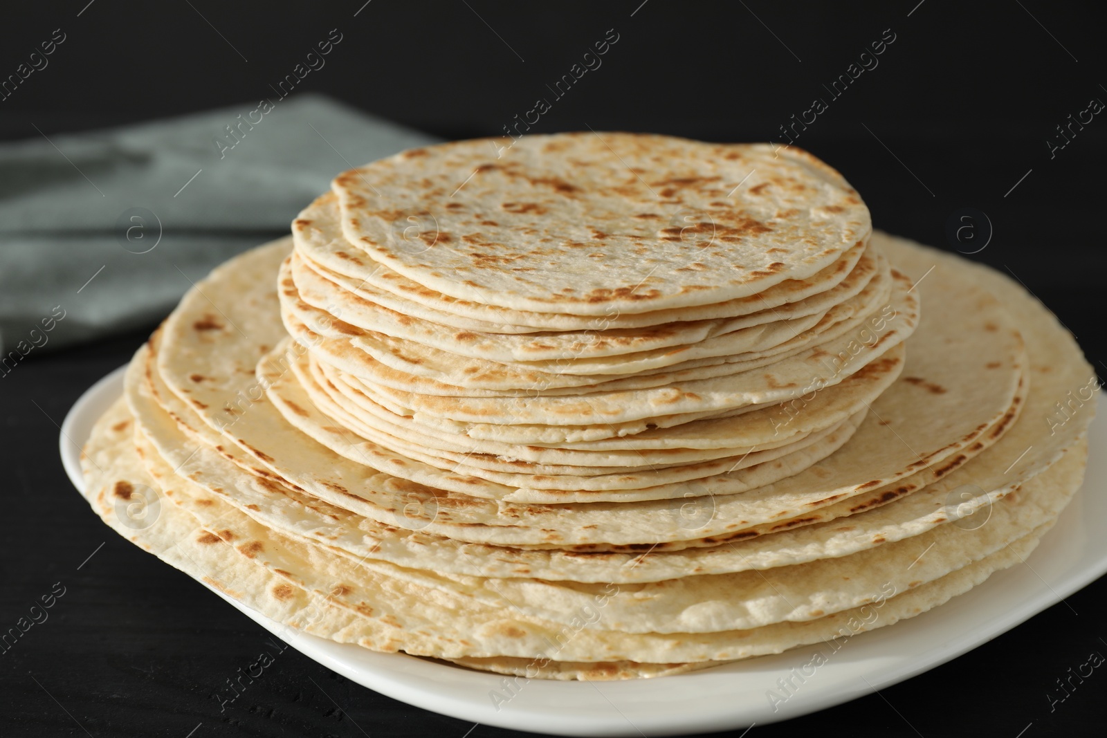 Photo of Many tasty homemade tortillas on black wooden table, closeup