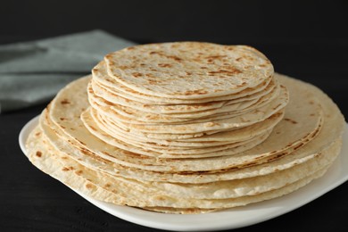 Photo of Many tasty homemade tortillas on black wooden table, closeup