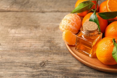 Bottle of tangerine essential oil and fresh fruits on wooden table, space for text