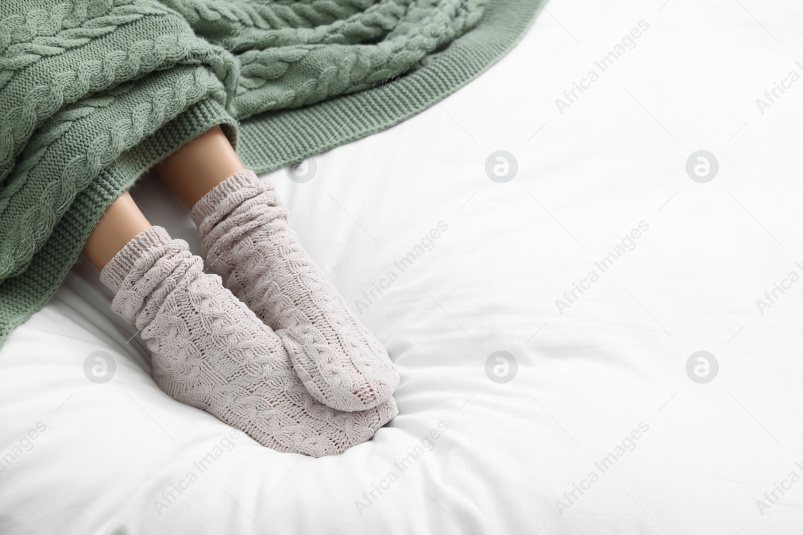 Photo of Woman wearing warm socks in comfortable bed, closeup. Space for text