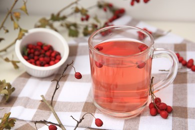 Photo of Cup with hawthorn tea and berries on table, closeup. Space for text