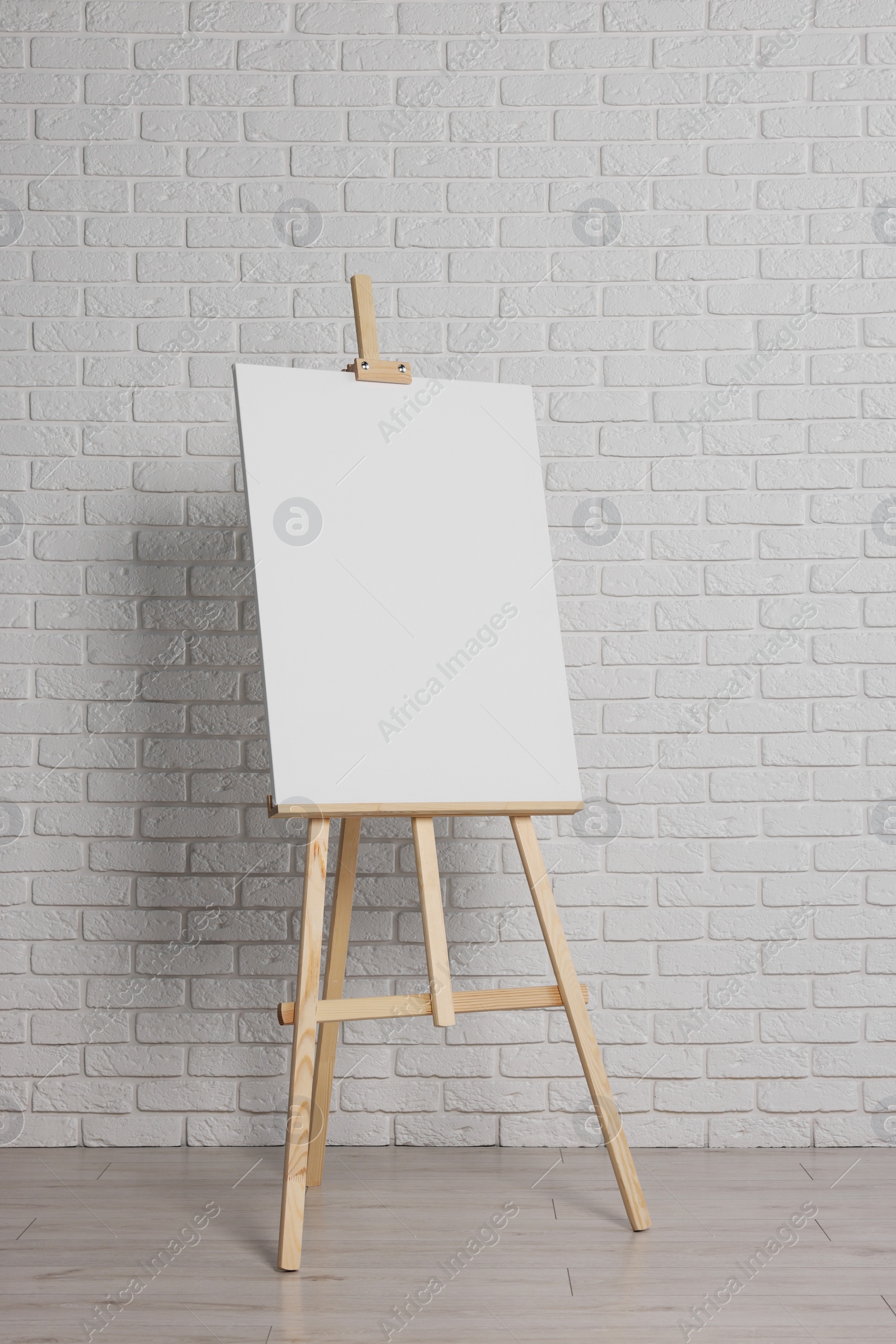 Photo of Wooden easel with blank canvas near white brick wall indoors