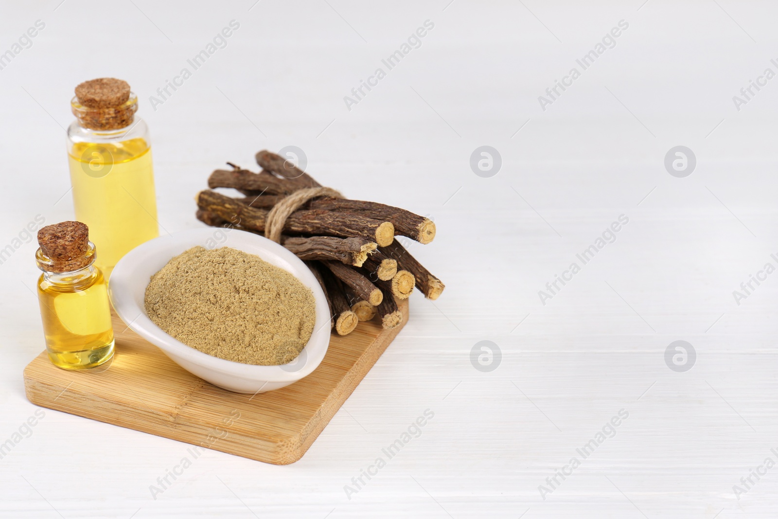 Photo of Dried sticks of licorice roots, bottles with essential oil and powder on white wooden table. Space for text